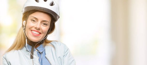 Young woman with bike helmet and earphones with crossed arms confident and happy with a big natural smile laughing - Photo, Image