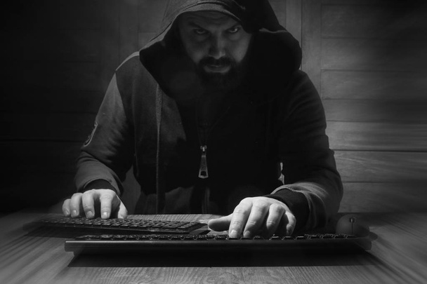Der Hacker in der Haube sitzt und arbeitet hinter dem Computer - Foto, Bild