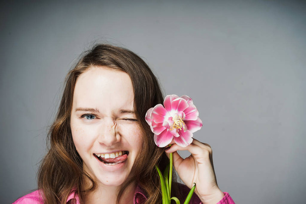 smiling blue-eyed girl in a pink shirt holding a fragrant flower - Фото, изображение