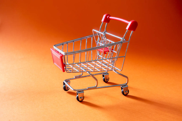 Nahaufnahme Einkaufswagen auf orangefarbenem Hintergrund mit Kopierraum - Foto, Bild