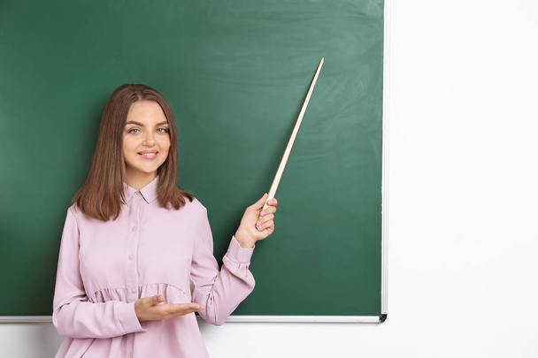 Portret van vrouwelijke leraar met de aanwijzer in de buurt van schoolbord in de klas - Foto, afbeelding