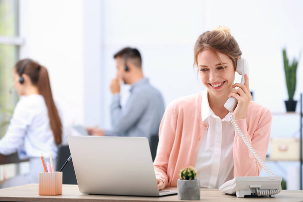 Recepcionista femenina hablando por teléfono en el escritorio en la oficina
 - Foto, Imagen