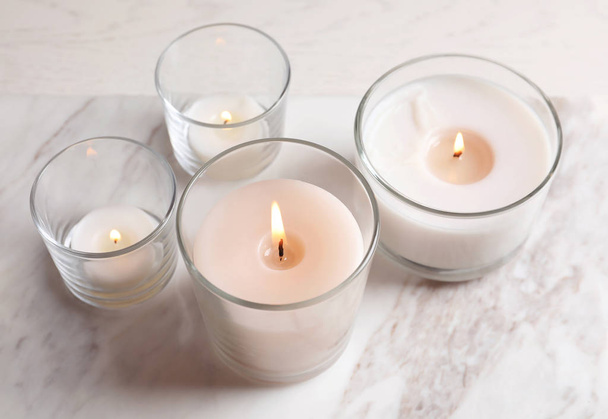 Burning candles in glasses on marble table - Φωτογραφία, εικόνα
