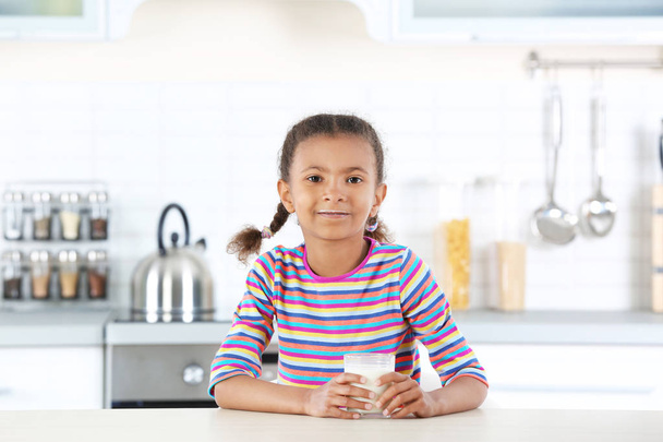 Adorable chica afroamericana con vaso de leche en la cocina
 - Foto, Imagen