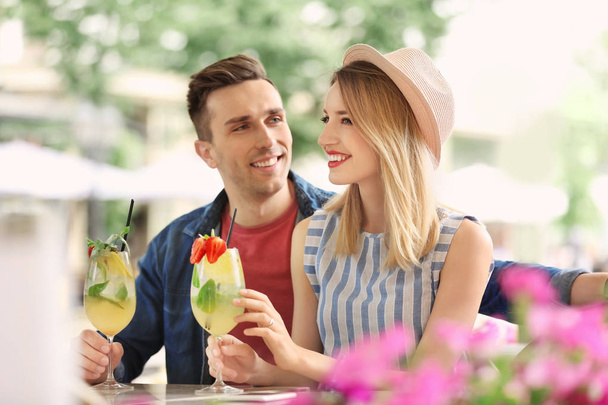 Jong (echt) paar met glazen lekkere limonade in openlucht café - Foto, afbeelding