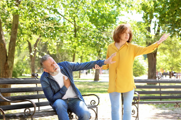 Woman helping mature man suffering from heart attack on bench in park - Foto, imagen