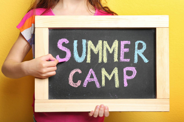 Girl writing SUMMER CAMP with colorful chalk on blackboard, closeup - Foto, imagen