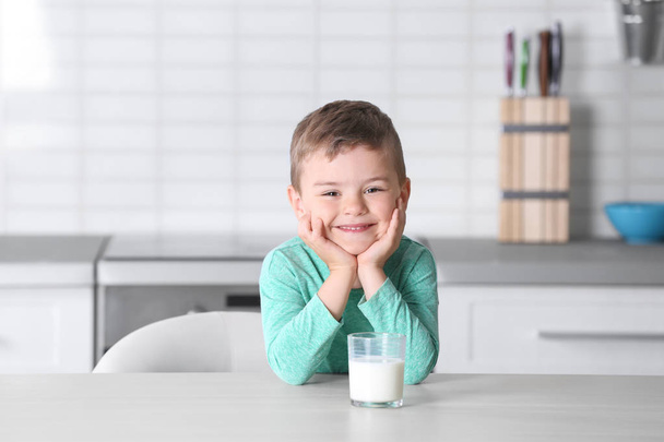 Mignon petit garçon avec verre de lait à table dans la cuisine
 - Photo, image