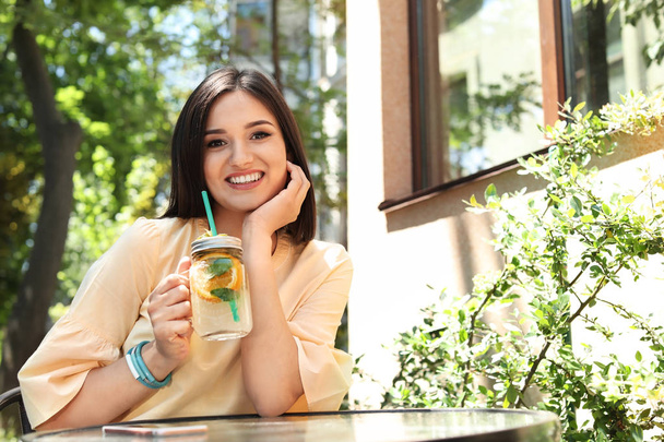 Young woman with mason jar of tasty natural lemonade at table, outdoors. Detox drink - Foto, Imagem