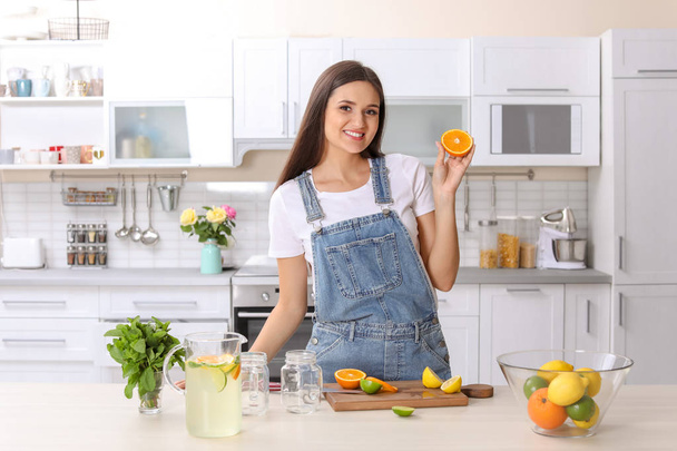 Young woman preparing lemonade on table in kitchen. Natural detox drink - Zdjęcie, obraz