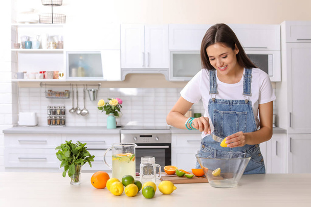 Young woman preparing lemonade on table in kitchen. Natural detox drink - Photo, image