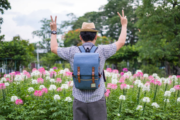 Touristenrucksack junger Mann steht für Siegesvorstellungen Handzeichen. im Spinnenblumengarten. auf Reisen in den Ferien. Es ist eine wunderschöne natürliche Vegetation - Foto, Bild