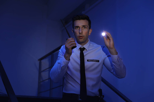 Male security guard with flashlight and portable radio transmitter in dark room - Valokuva, kuva