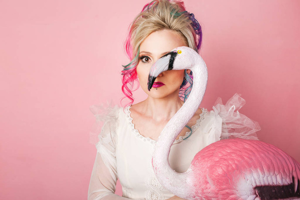 Stylish and beautiful woman with colored hair. Hugging a pink Flamingo figure. - 写真・画像