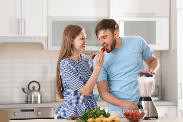 Cute young couple preparing delicious milk shake in kitchen - Foto, afbeelding