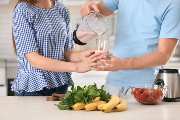 Young man pouring delicious milk shake into glass for his girlfriend in kitchen - Zdjęcie, obraz