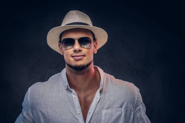 Nahaufnahme eines gut aussehenden bärtigen Mannes in weißem Hemd, Panamahut und Sonnenbrille. isoliert auf dunklem Hintergrund. - Foto, Bild