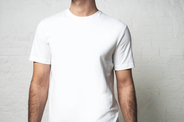Young guy in white blank t-shirt, horizontal studio close-up, empty wall - Foto, afbeelding