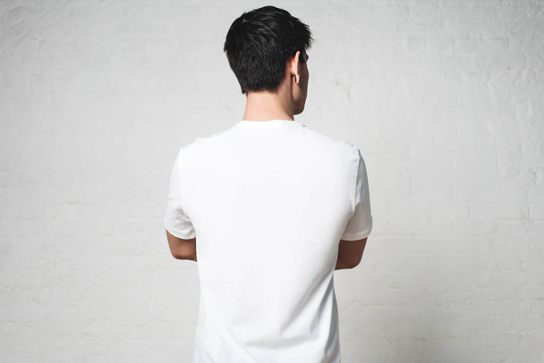 Young athletic guy in blank white t-shirt, back side, horizontal studio portrait, empty wall - Photo, image
