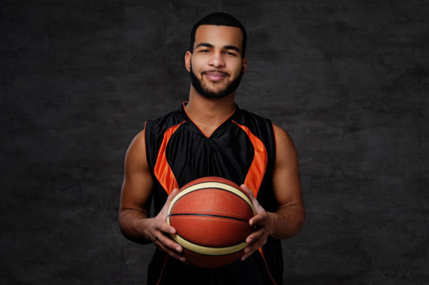 Jeune joueur de basket afro-américain souriant en tenue de sport isolé sur fond sombre
.  - Photo, image