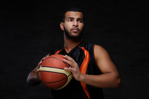 Portret młodego African-American koszykarz w sportowej na białym tle nad ciemnym tle.  - Zdjęcie, obraz