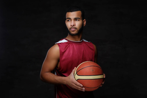 Portrait d'un sportif afro-américain. Basketball joueur en vêtements de sport avec une balle sur un fond sombre
. - Photo, image