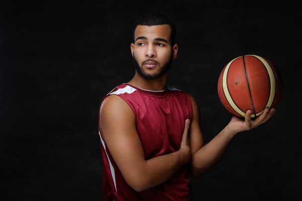 Portrait of an Afro-American sportsman. Basketball player in sportswear with a ball on a dark background. - Fotoğraf, Görsel