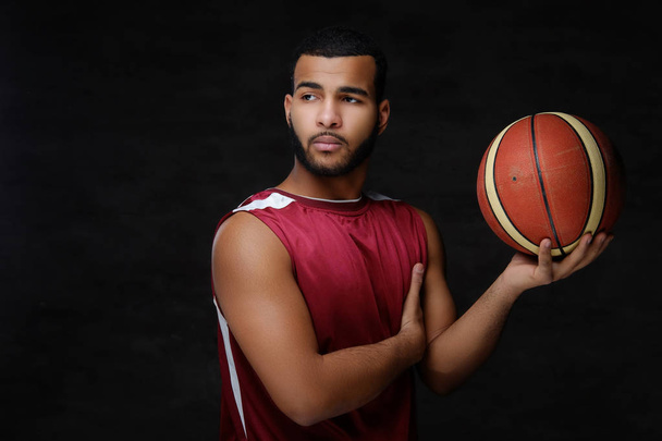 Portrait of a young African-American basketball player in sportswear isolated over dark background.  - Photo, Image