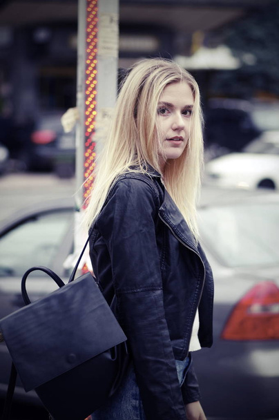 Красивая блондинка позирует на улице. Девушка одета в черную кожаную куртку и белый свитер
. - Фото, изображение
