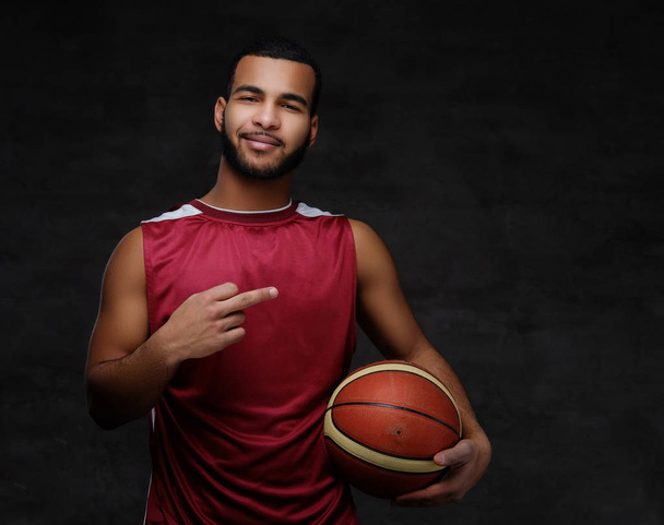 Retrato de um desportista afro-americano. Jogador de basquete em sportswear com uma bola em um fundo escuro
. - Foto, Imagem