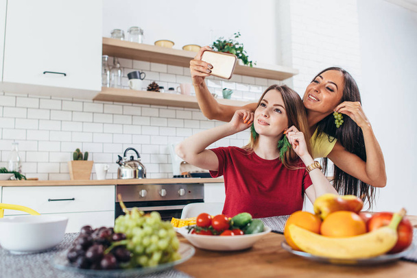 Mulheres comendo brincando com legumes na cozinha se divertindo e tirando selfie
 - Foto, Imagem