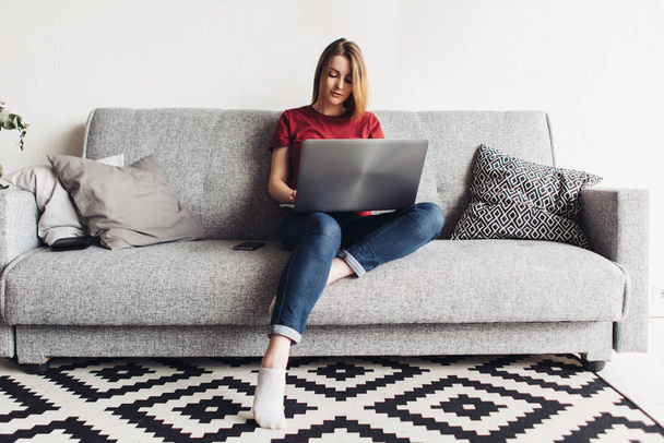Mujer usando ordenador portátil sentado en el sofá en la sala de estar
 - Foto, imagen