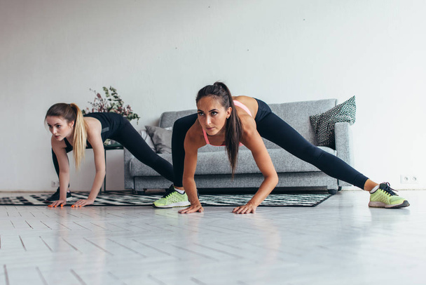 Dos chicas en forma haciendo ejercicios en casa realizando embestidas laterales en casa
. - Foto, imagen