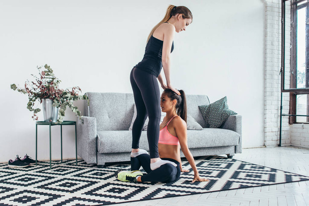 Woman helping friend in leg stretching workout at home - Zdjęcie, obraz
