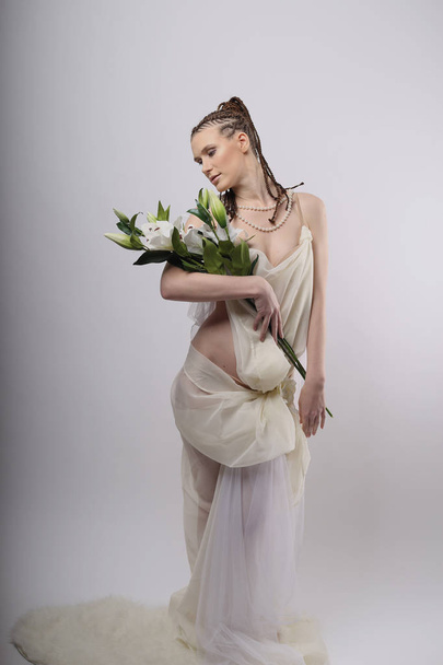 meisje met exotische kapsel op witte achtergrond met bloemen lily, witte jurk, Griekse stijl, Afrikaanse kapsel - Foto, afbeelding