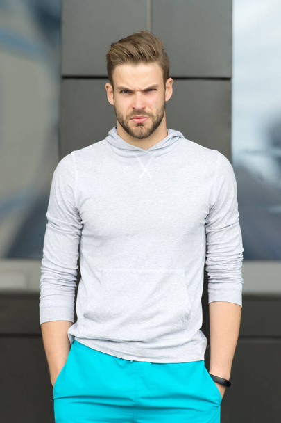 Sport fashion concept. Guy bearded and attractive cares about appearance. Man with bristle on serious face in sporty wear, urban background. Man with beard or unshaven guy in stylish sport clothes - Foto, imagen