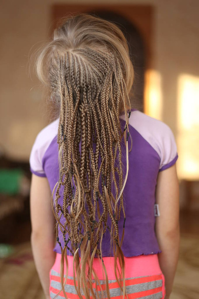 kleines Mädchen mit einem Haarschnitt aus afrikanischen Zöpfen, amerikanischen Zöpfen, dünn, die Arbeit eines Zauberers, eine Frisur im Prozess der Socken, Hintergrund für Text - Foto, Bild