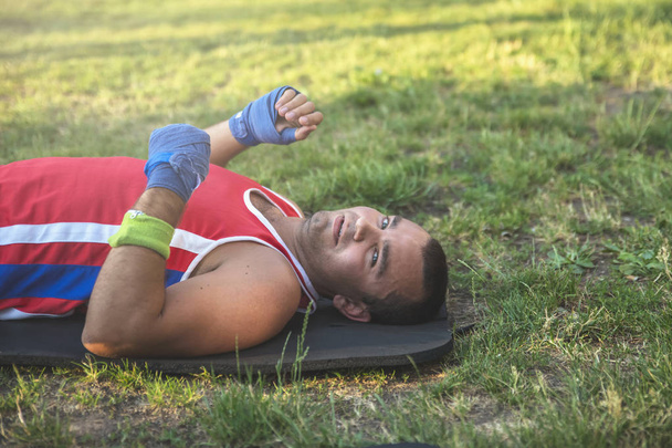 Молодий спортсмен лежить на спині на траві під час паузи на спортивній підготовці
 - Фото, зображення