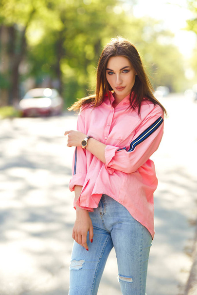 Retrato de mujer joven y hermosa en ropa casual en la calle. vestido con una camisa rosa y jeans. concepto primavera / verano. tiempo de relax. chica con ojos azules. Disfruta del atardecer callejero
 - Foto, imagen