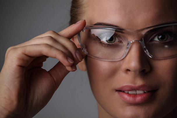 Όμορφη γυναίκα με διαφανή φουτουριστικό γυαλιά σε γκρίζο φόντο - Φωτογραφία, εικόνα