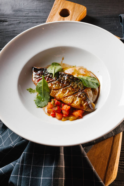 Жареная рыба подается с соусом и овощным рагу в белой тарелке
 - Фото, изображение