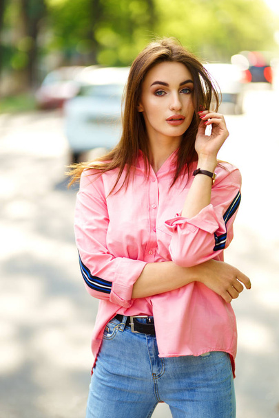 Портрет молодой и красивой женщины в повседневной одежде на улице. одетый в розовую рубашку и джинсы. весна / лето. Расслабься девушка с голубыми глазами. Наслаждайтесь уличным закатом
 - Фото, изображение