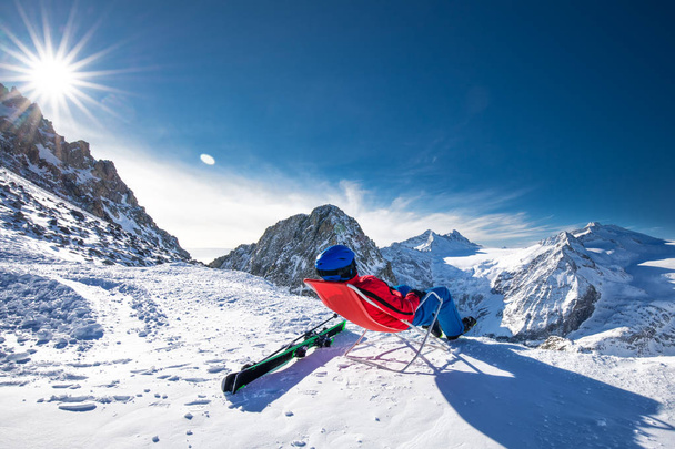Jeune skieur heureux et attrayant assis au sommet des montagnes profitant de la vue depuis le glacier Presena, Tonale, Italie
. - Photo, image