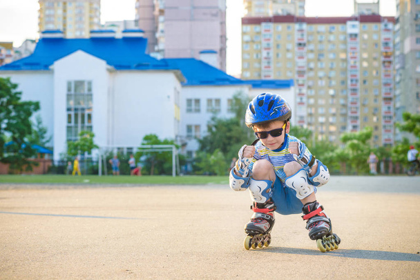 Маленький хлопчик катається на роликах влітку в парку. Щаслива дитина в шоломі вчиться кататися на ковзанах
. - Фото, зображення
