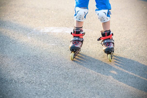 夏の公園でローラー スケートを学ぶ少年。子供たちの安全なローラー スケートに乗るのための保護パッドを身に着けています。子供のためのアクティブなアウトドア スポーツ。スケートのクローズ アップ表示. - 写真・画像