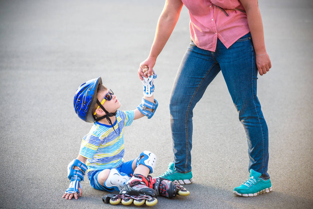 Preschooler falls over while rollerblading with mother in the park. Little boy learning to roller skate. Children wearing protection pads for safe ride. Active outdoor sport for kids. - Zdjęcie, obraz