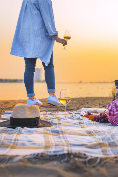 Romantic picnic on the beach by the sea. Girl with a glass of wine in hands and sunset. Good weekend. Copy space - Foto, imagen