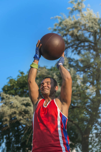 Молодой спортсмен выполняет спортивные упражнения с мячом на открытом воздухе
 - Фото, изображение