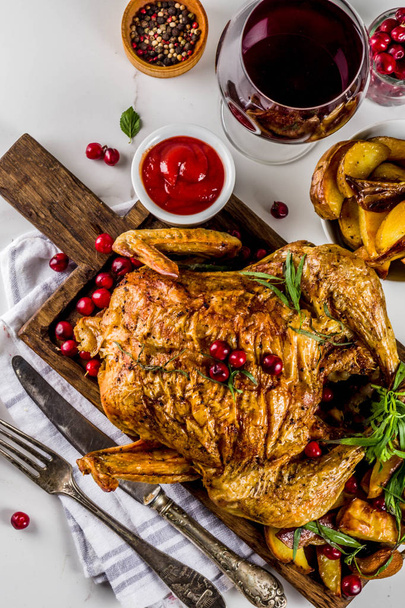 Рождество, праздничная еда, жареная курица с клюквой и травами, подается с жареными овощами, вином из ягод и соусами на белом мраморном столе, вид сверху
 - Фото, изображение