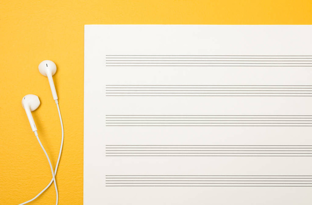 Beyaz kulaklık ve boş müzik kağıt levha canlı sarı zemin üzerine. - Fotoğraf, Görsel